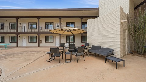 A patio with a table and chairs and a yellow umbrella.