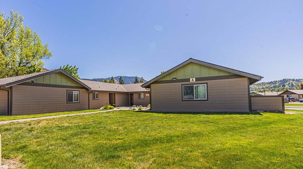 the exterior of a home with a grassy yard and two houses in the background