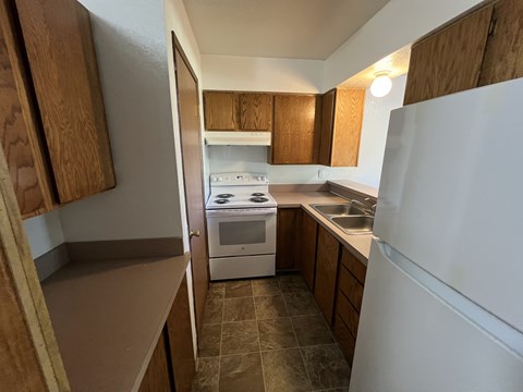 A kitchen with a white refrigerator, a white oven, and wooden cabinets.