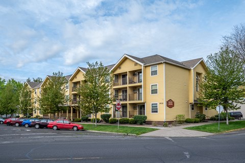 A yellow apartment building with a red car parked in front.
