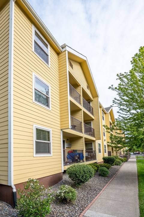 A yellow building with a balcony and a small garden in front.