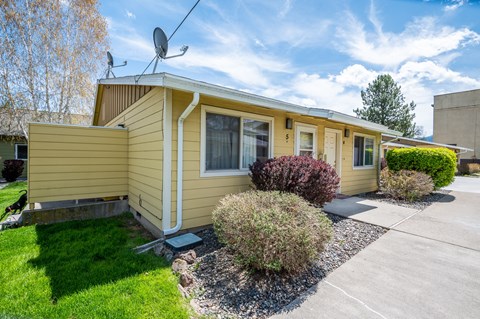 the front of a yellow house with a lawn and a driveway