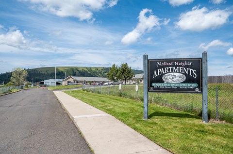 A sign for Mallard Heights Apartments is displayed in front of a road.