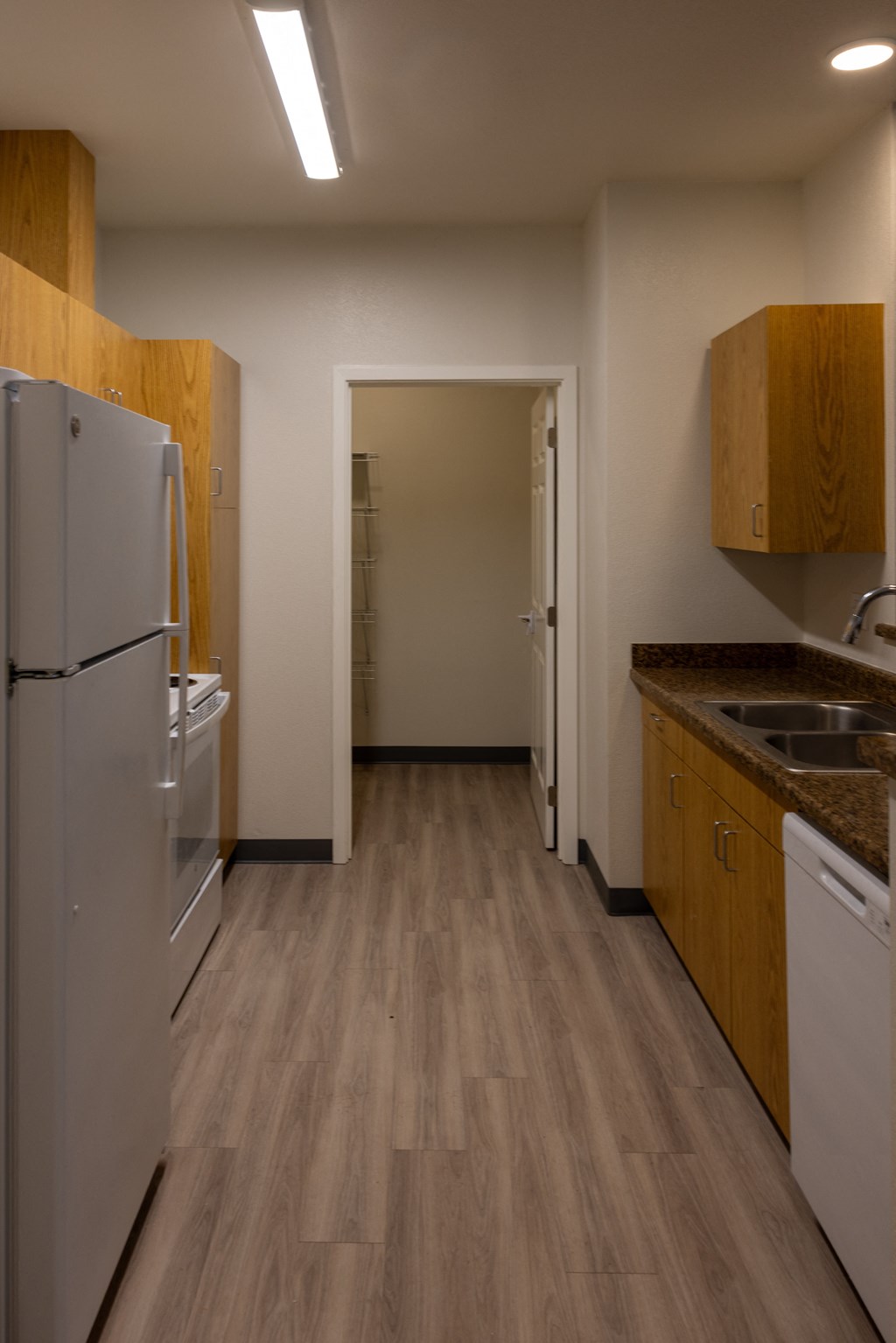 a kitchen with white appliances and wooden cabinets and a door to a hallway