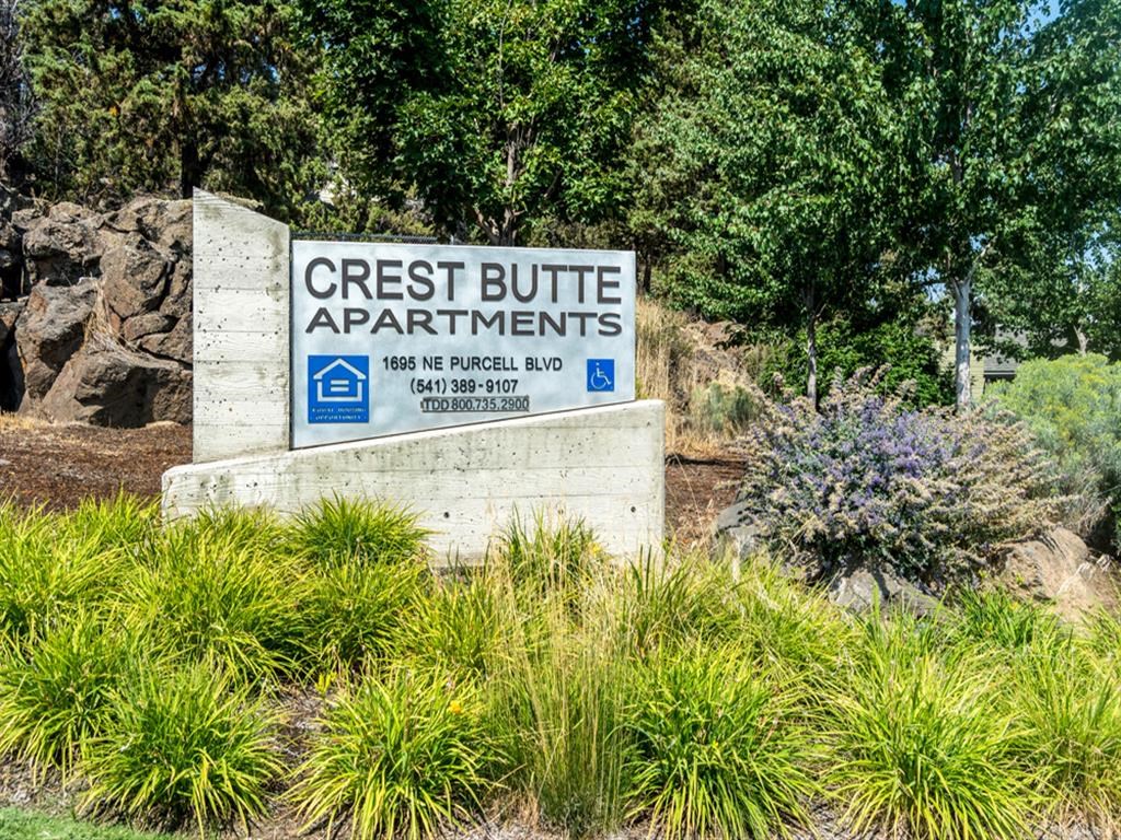 a sign for the crest butte apartments in front of trees and plants