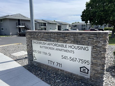 A sign for Sagerbrush Affordable Housing stands in front of apartment buildings.