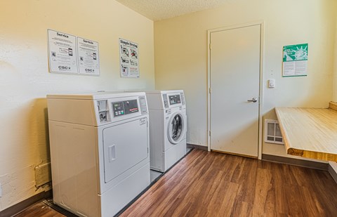 a laundry room with two washer and dryers and a door to a kitchen