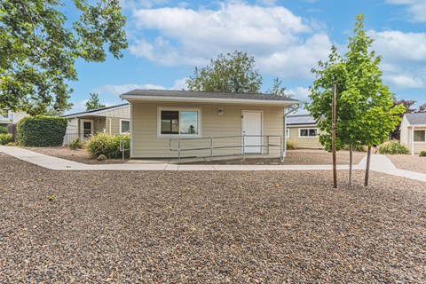 a small tan house with a gravel driveway and trees