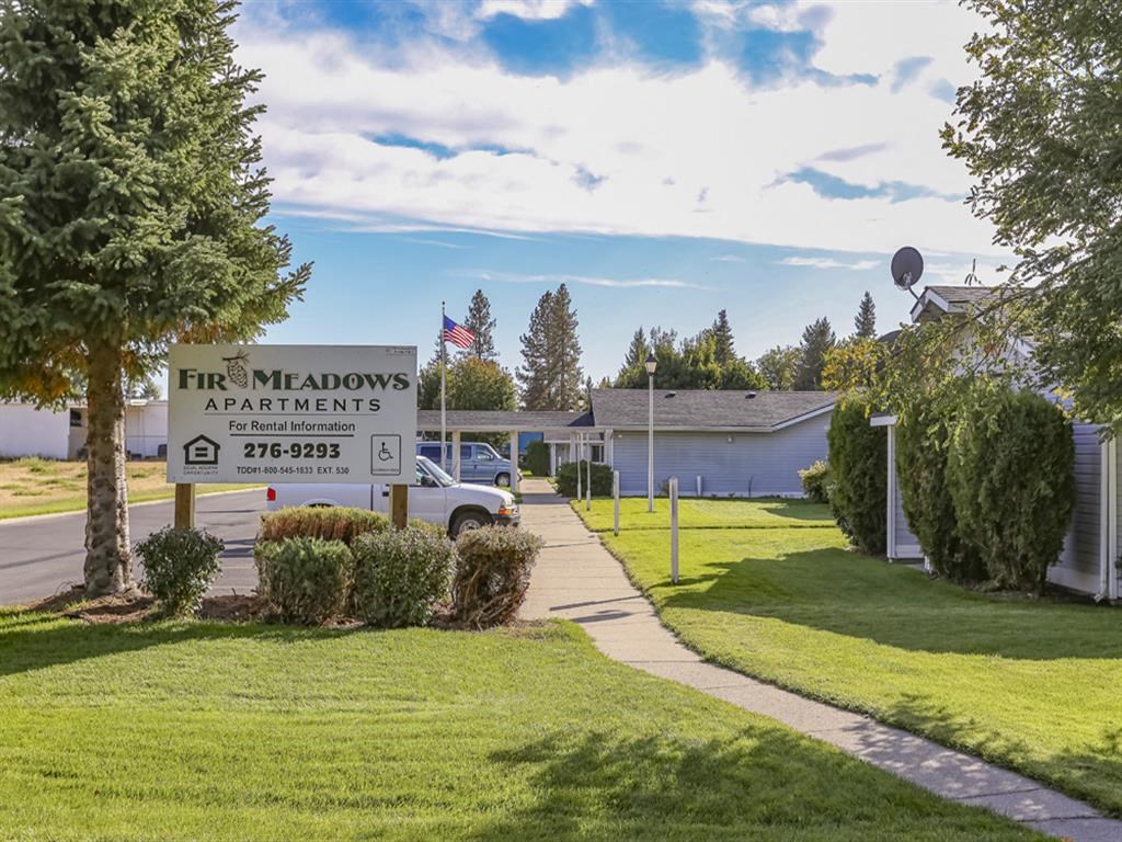 a sign in front of a house with a lawn and a driveway