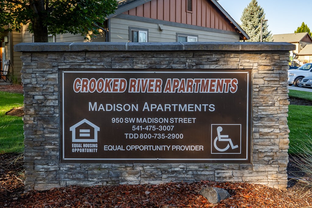 A sign for Crooked River Apartments with a phone number and address.