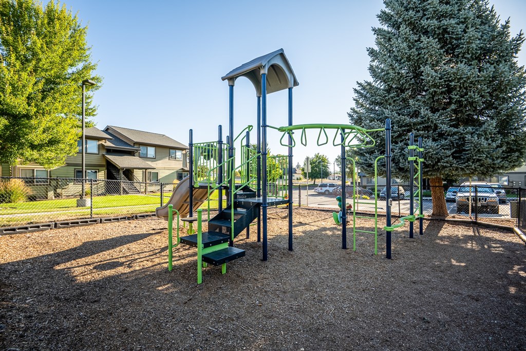 A playground with a green slide and a brown swing set.