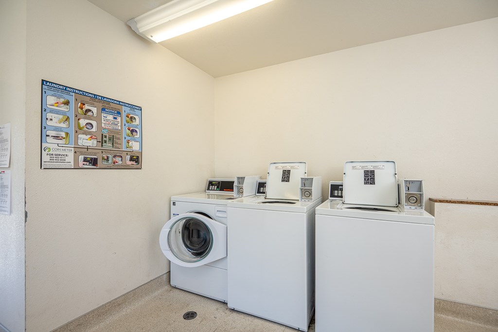 A room with a poster on the wall and three washing machines.