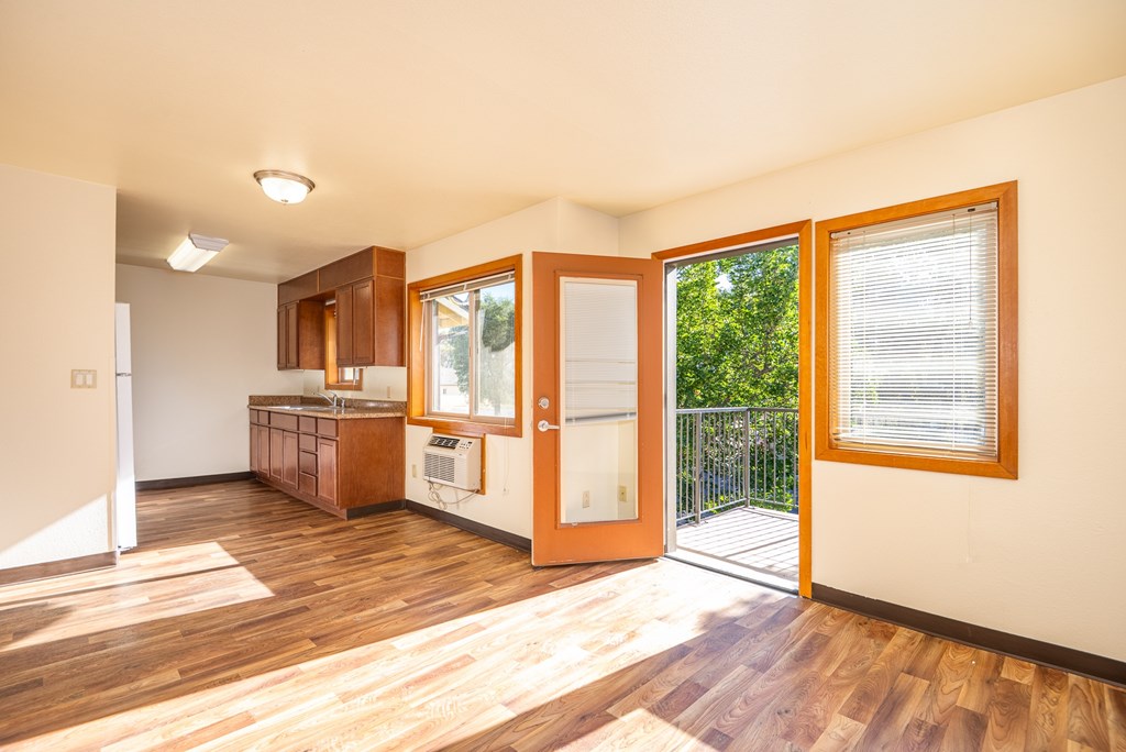 A room with wooden floors and a kitchen area with a refrigerator, sink, and cabinets.