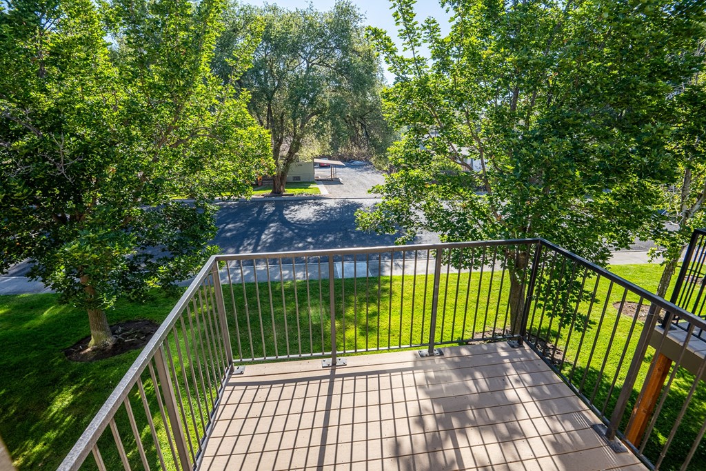A balcony with a metal railing and a tiled floor overlooks a green lawn and trees.