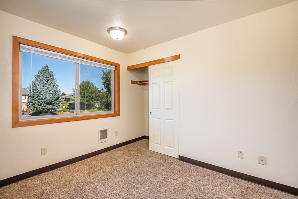 A room with a white door and a window with a view of trees.