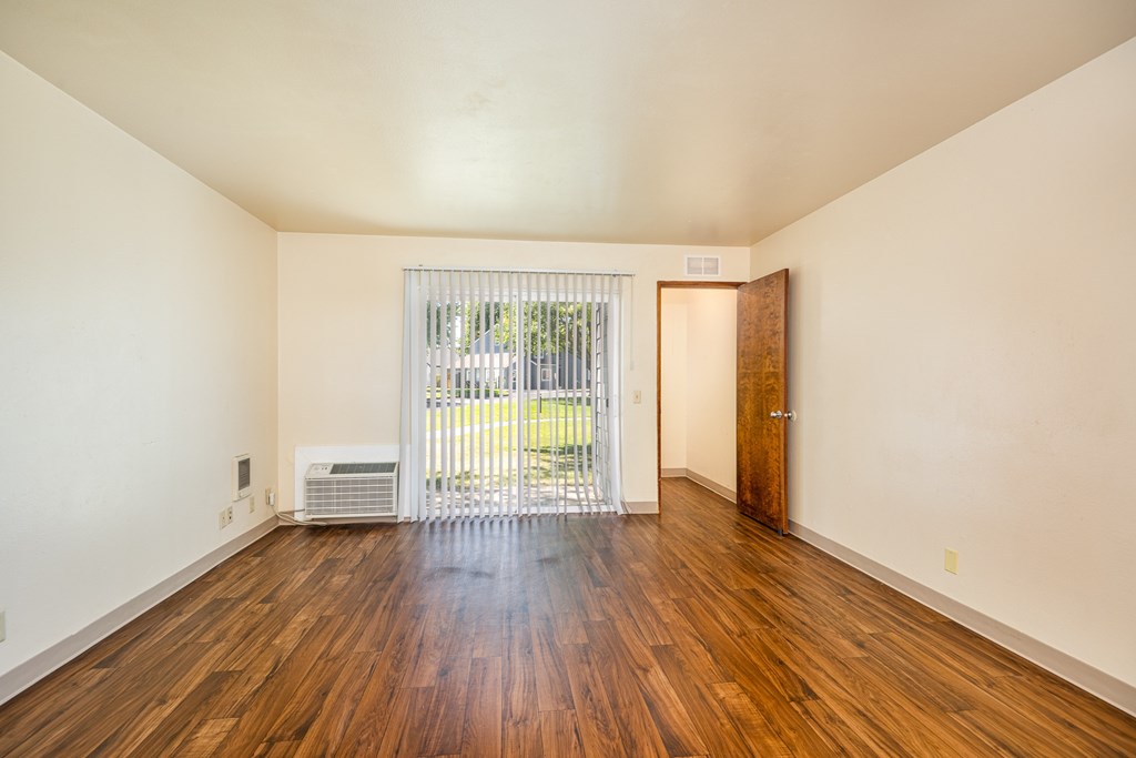 A room with wooden floors and a sliding glass door leading to a backyard.