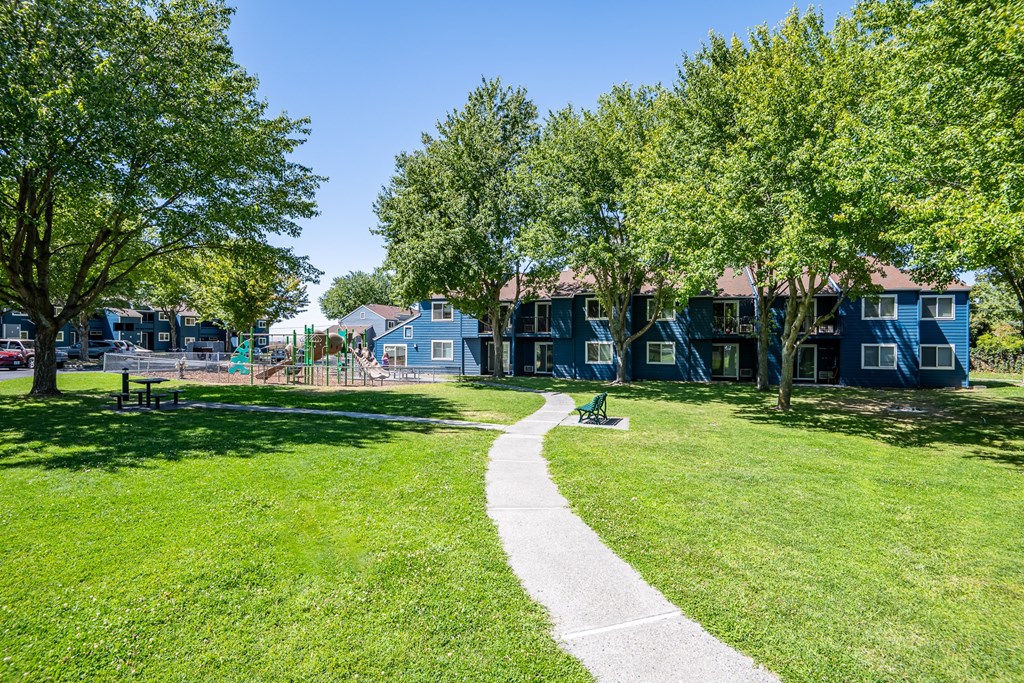 A park with a walking path, grass, and trees.