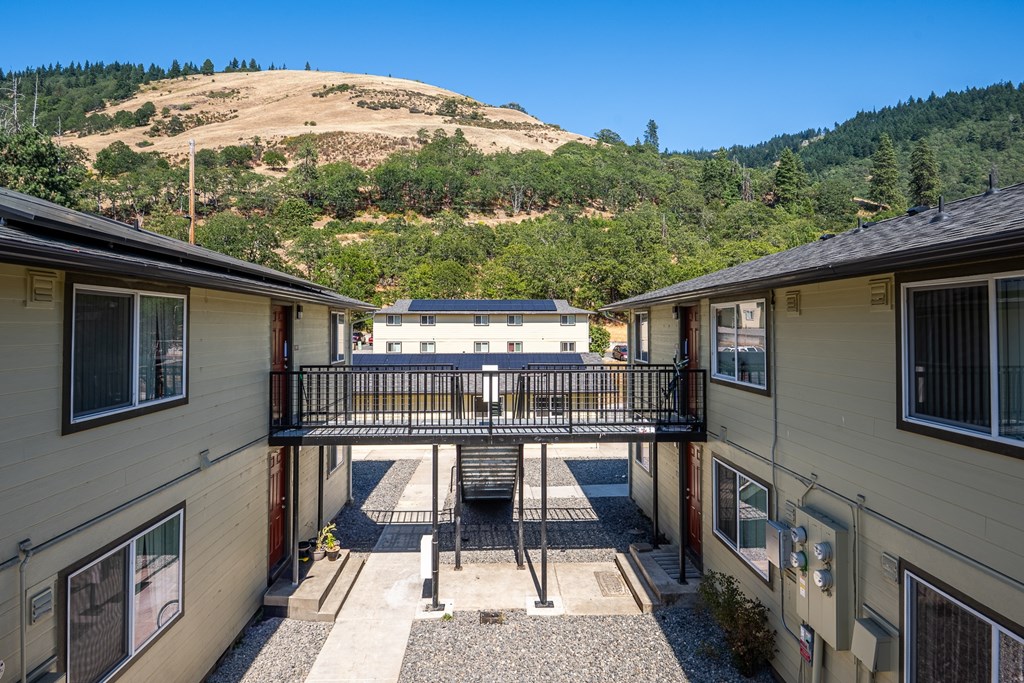 A view of a courtyard between two houses with a hill in the background.
