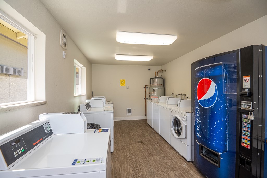A Pepsi vending machine sits in a laundromat next to washing machines.