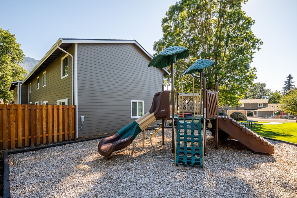 A playground with a slide and a wooden fence in the background.