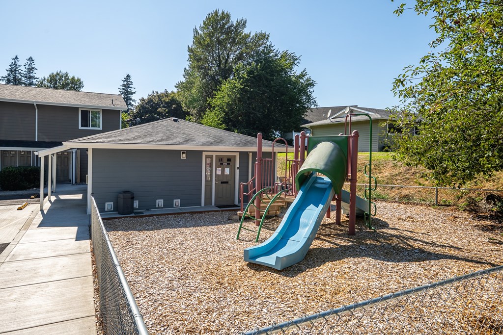 A playground with a green slide and a grey building in the background.