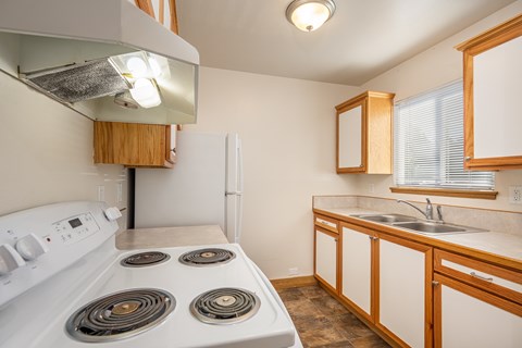 A white stove with four burners is in a kitchen with wooden cabinets.