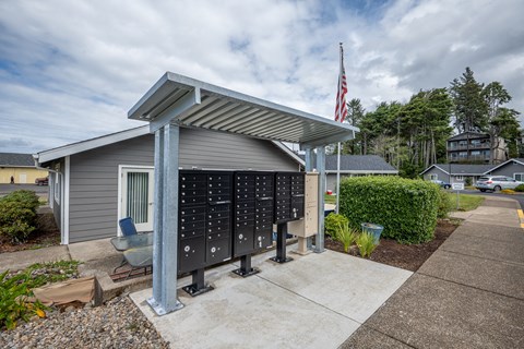 A grey building with a flag on top and a row of mailboxes in front.