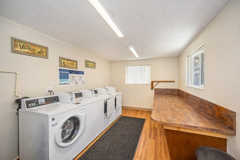 A laundromat with washers and dryers lined up on the left and a bench on the right.