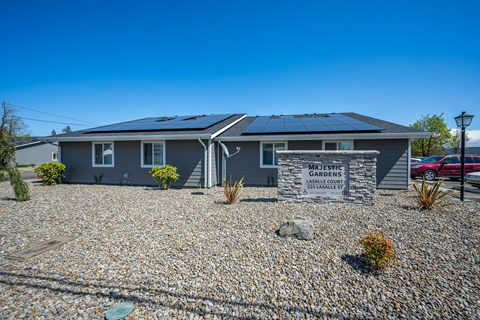 A house with solar panels on the roof and a sign that says "Majestic Gardens".