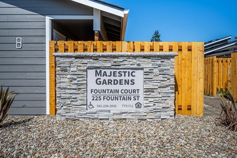 A sign for Majestic Gardens Fountain Court is displayed in front of a building.