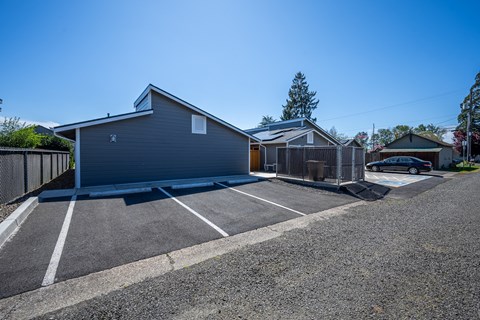 A parking lot with a grey building and a car parked in front.