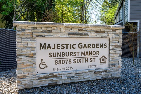 Majestic Gardens Sunburst Manor sign with a stone wall and a fence.