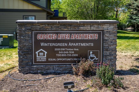 A sign for Crooked River Apartments is displayed in front of a building.