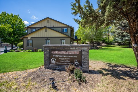 A sign for Grooked River Apartments sits in front of a building.