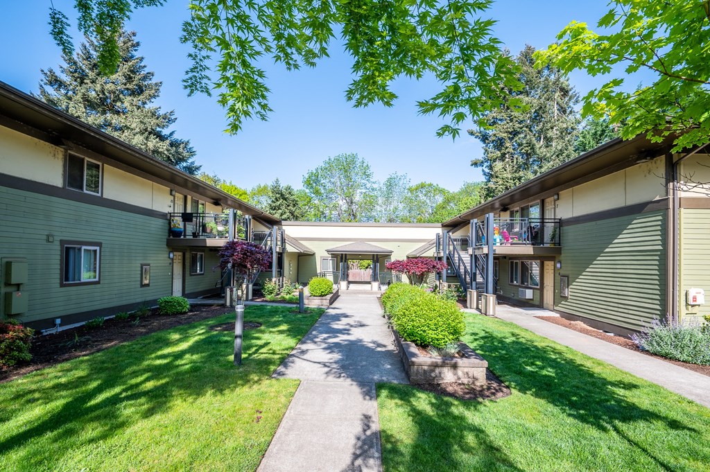 a walkway between two buildings with a lawn and trees