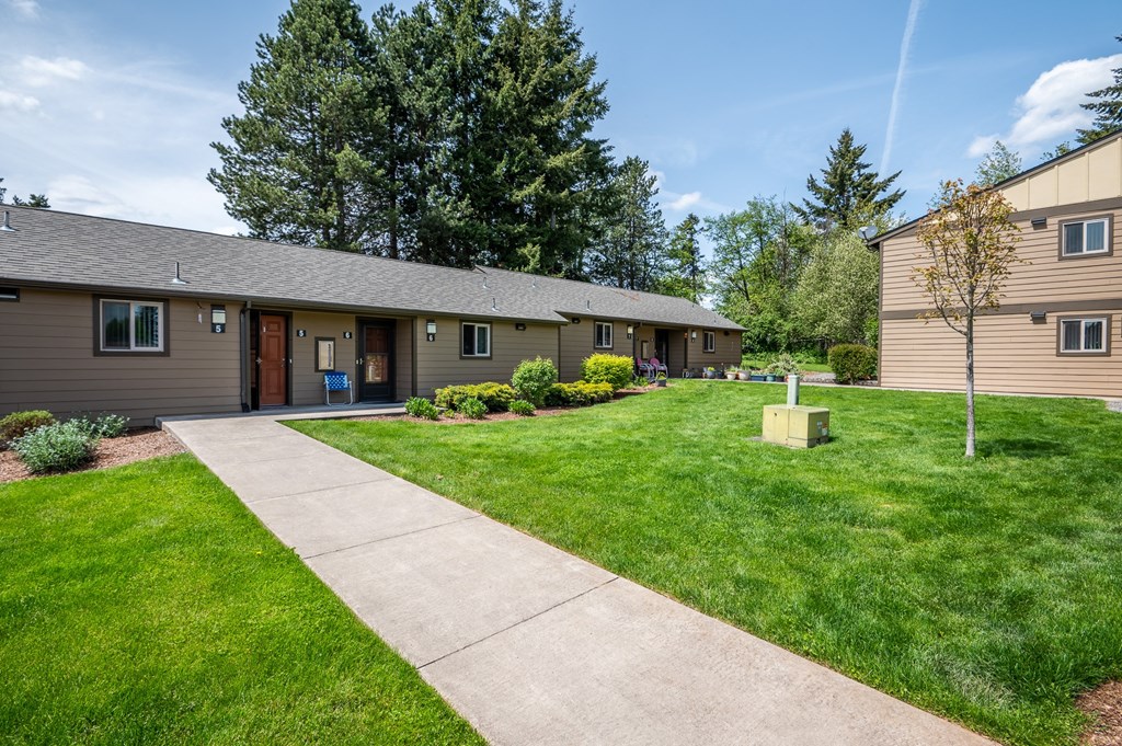 a sidewalk in front of a house with a lawn and trees