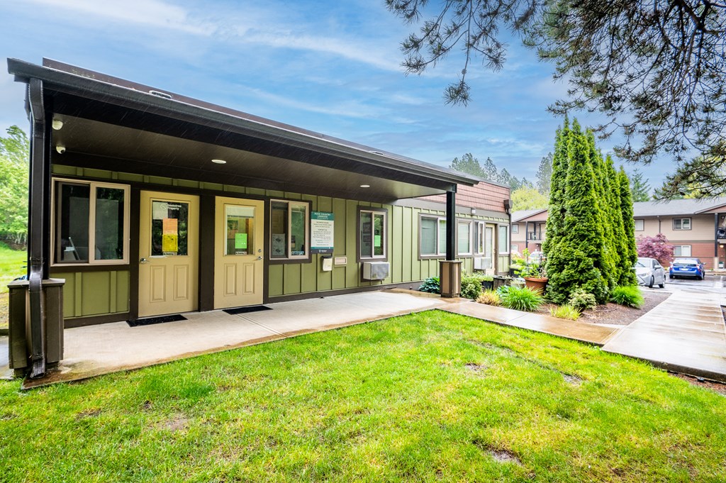 the front of a green house with a lawn and a driveway
