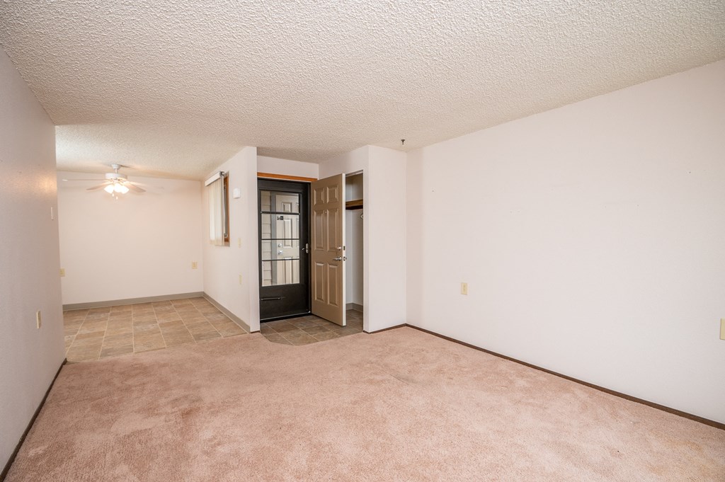 the living room and dining room of an apartment with carpet and white walls