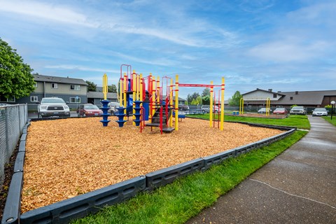 a playground in a mulch area next to a sidewalk