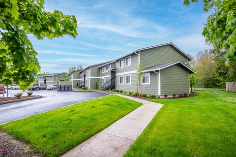 a green house with a sidewalk and a parking lot