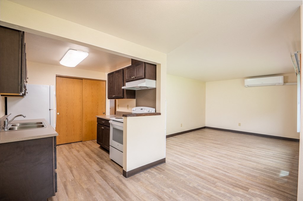 an empty living room and kitchen with a wood floor and white appliances