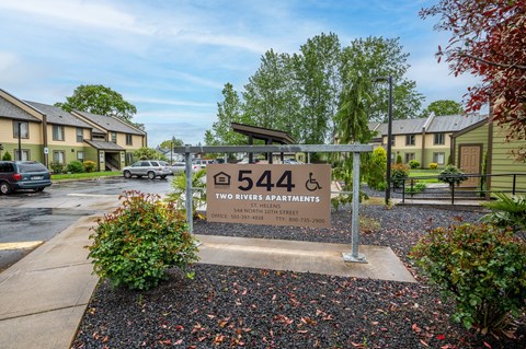 a sign in front of an apartment complex with trees and a parking lot