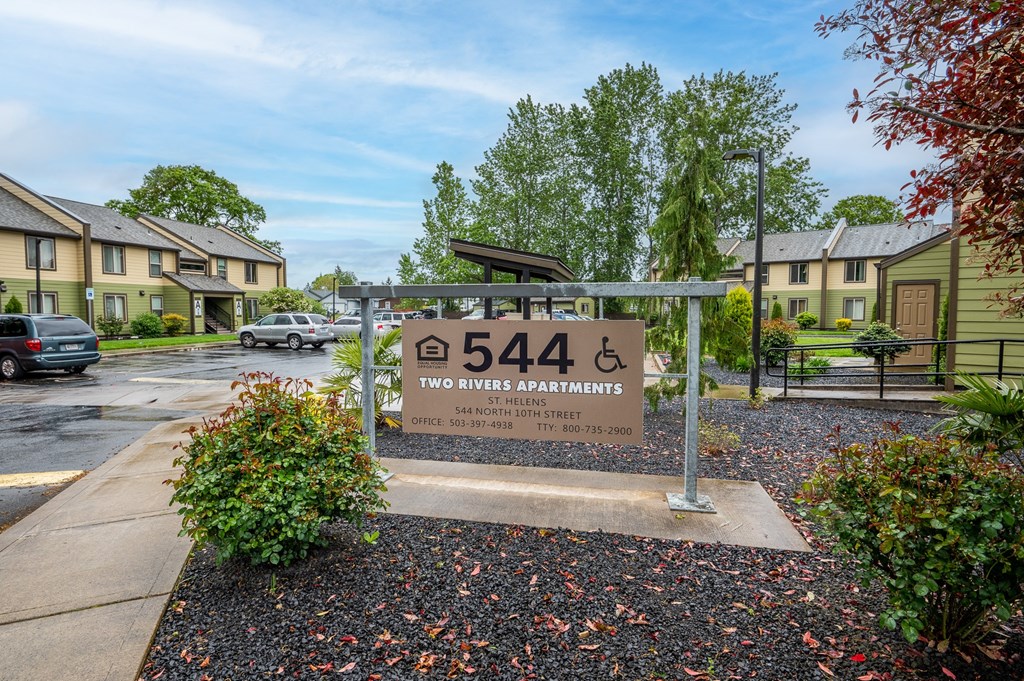 a sign in front of an apartment complex with trees and a parking lot