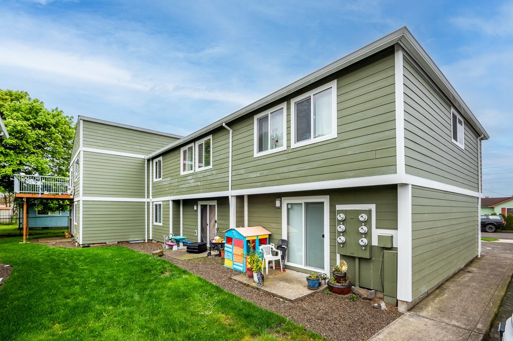 the exterior of a green house with a yard and a playhouse
