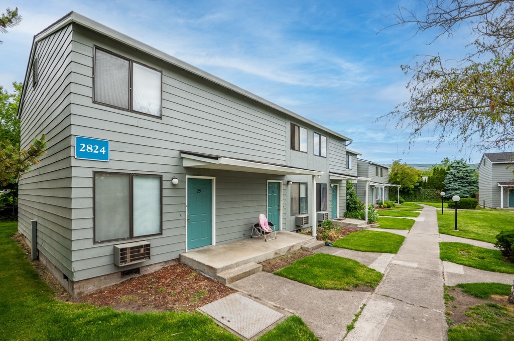 a gray house with blue doors and a sidewalk in front of it