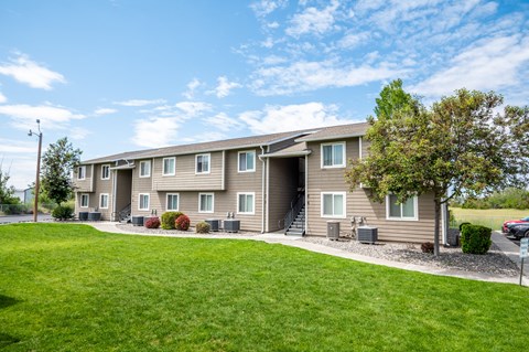 the outlook of a beige apartment building with a lawn and trees