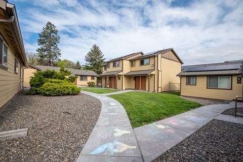 a pathway between a row of houses with grass and a sidewalk