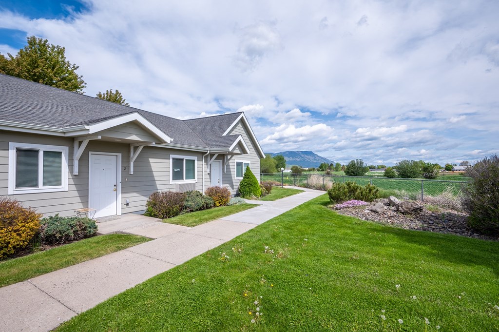 a gray house with a sidewalk and a field in the background