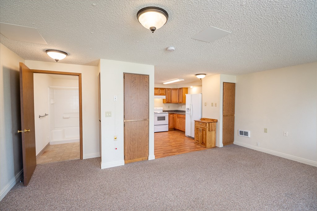 an empty living room with a kitchen in the background