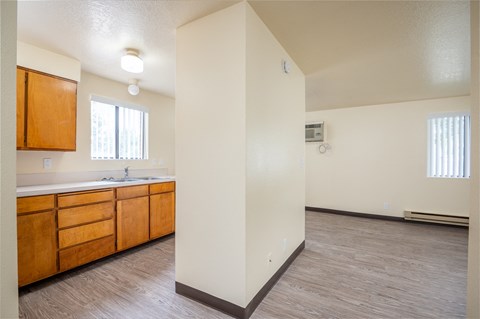 an empty living room and kitchen with wood flooring and white walls